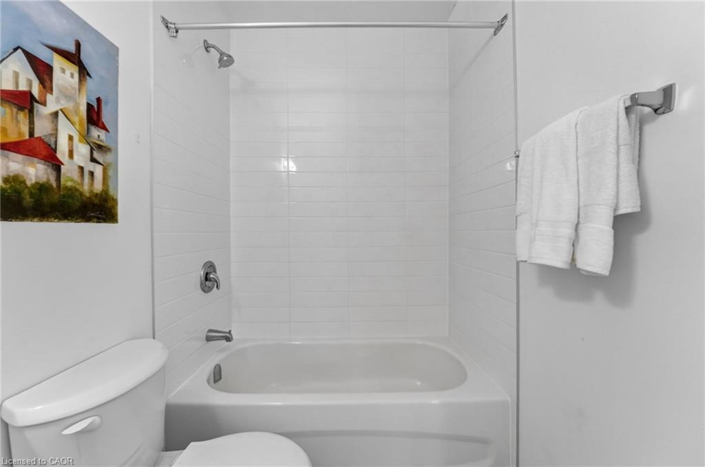 Bathroom with a white tiled tub and shower, toilet, and towels on a wall-mounted bar.