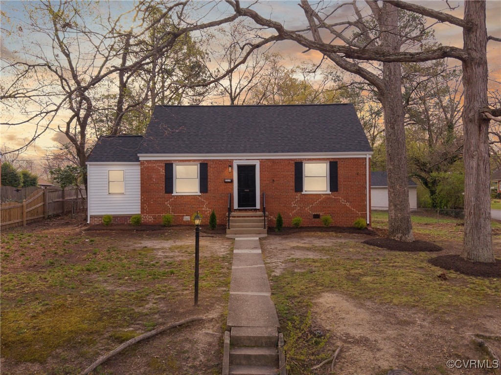 Red brick house with black shutters, white siding, and a walkway beneath mature trees.