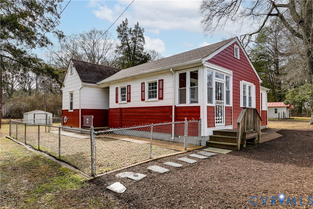 Red-and-white house with a fenced yard, small porch, and detached shed.
