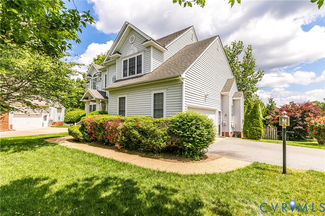 Light-sided, multi-gabled home with an attached garage, landscaped shrubs, and a curved walkway.