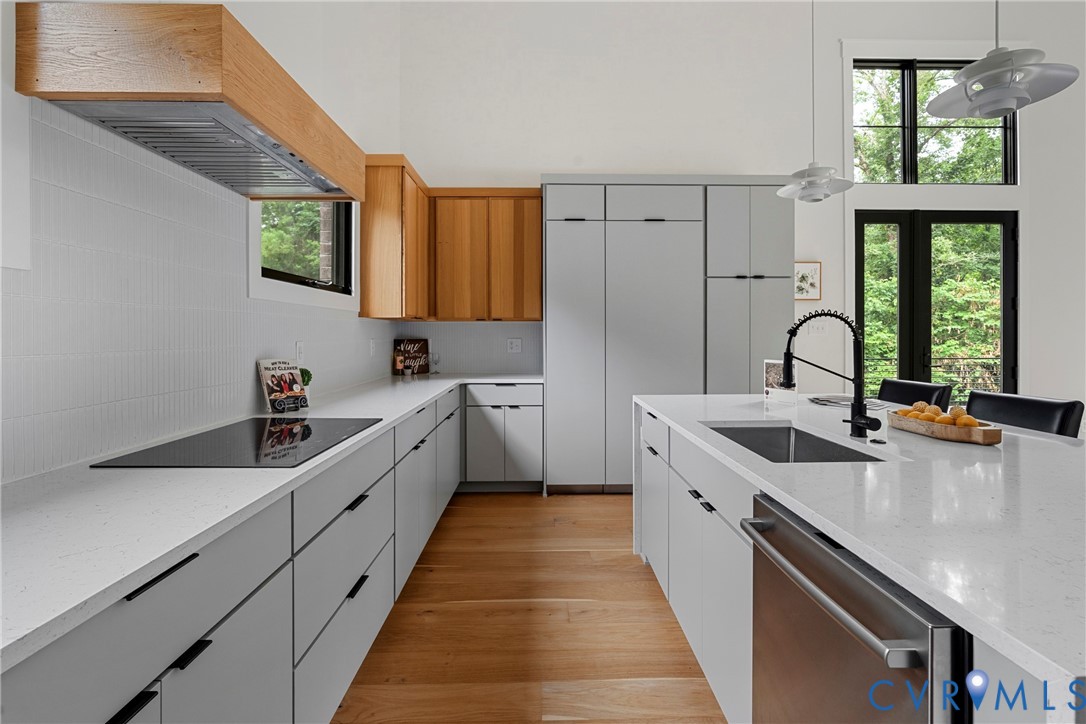 Modern kitchen with a large white island, warm wood cabinetry, and tall windows overlooking trees.