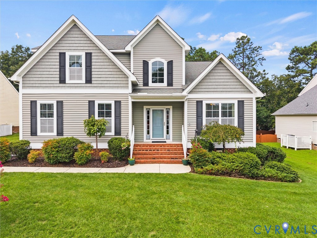 Gray two-story house with multiple gables, dark shutters, brick steps, and landscaped front lawn.