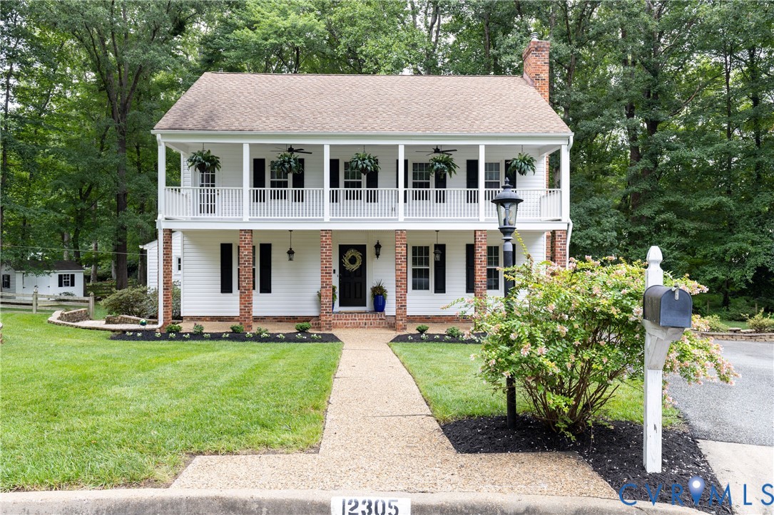 Two-story white house with brick porch columns, a covered balcony, and a front lawn beside the driveway.