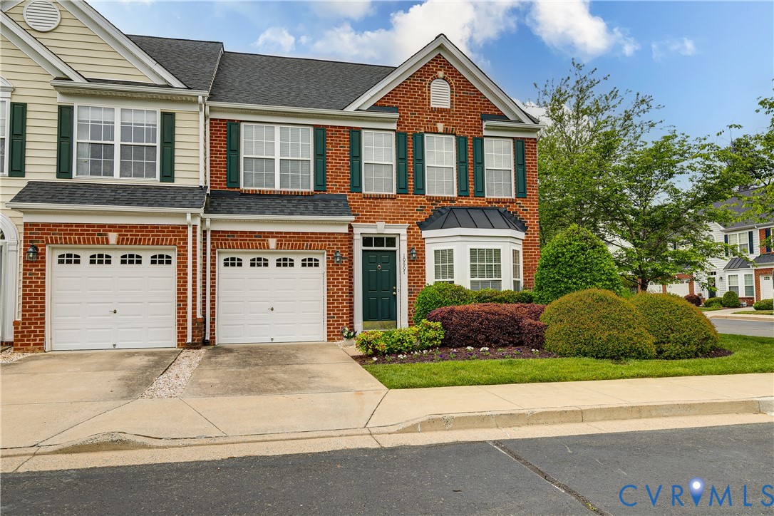 Two-story brick and cream-sided home with two garage doors, green shutters, and landscaped front yard.