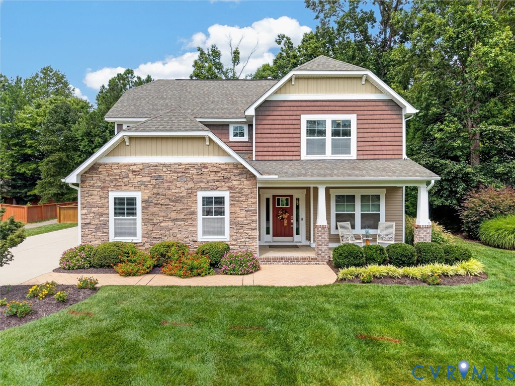 Two-story stone-and-red-sided house with a covered porch and landscaped front lawn.