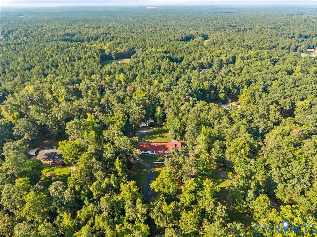 Aerial view of a red-roofed home surrounded by dense forest and neighboring homes.