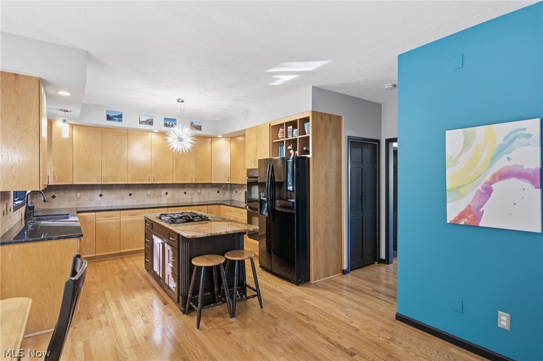 Kitchen with maple cabinets, a central island, black appliances, and a turquoise accent wall.