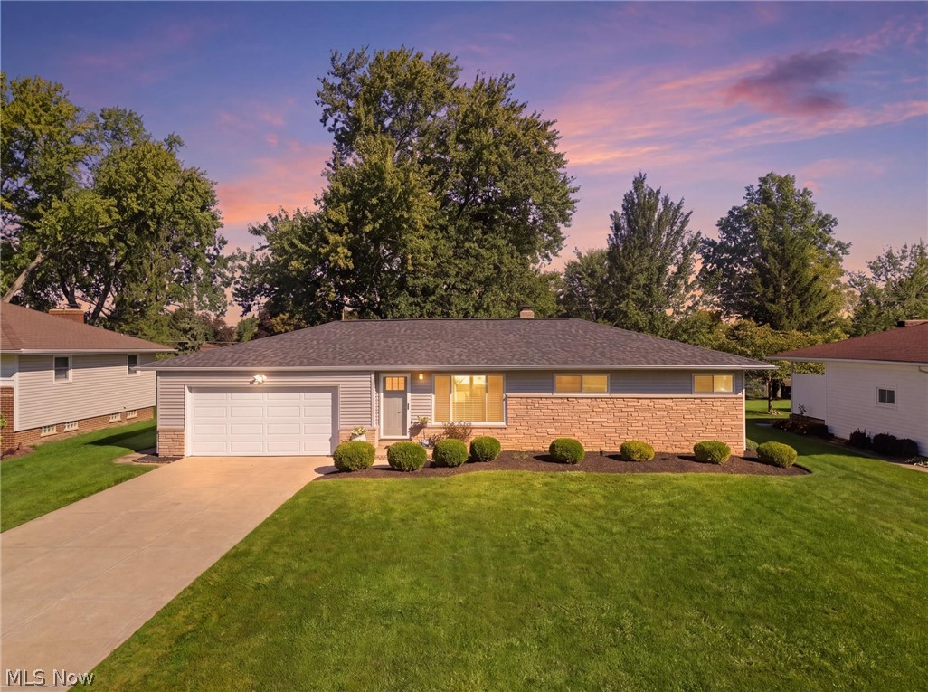 Single-story brick ranch home with an attached garage and broad lawn at sunset.
