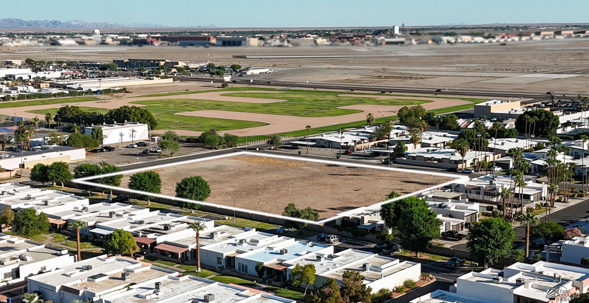 Aerial view of a vacant lot outlined in white, surrounded by homes, with distant mountains.