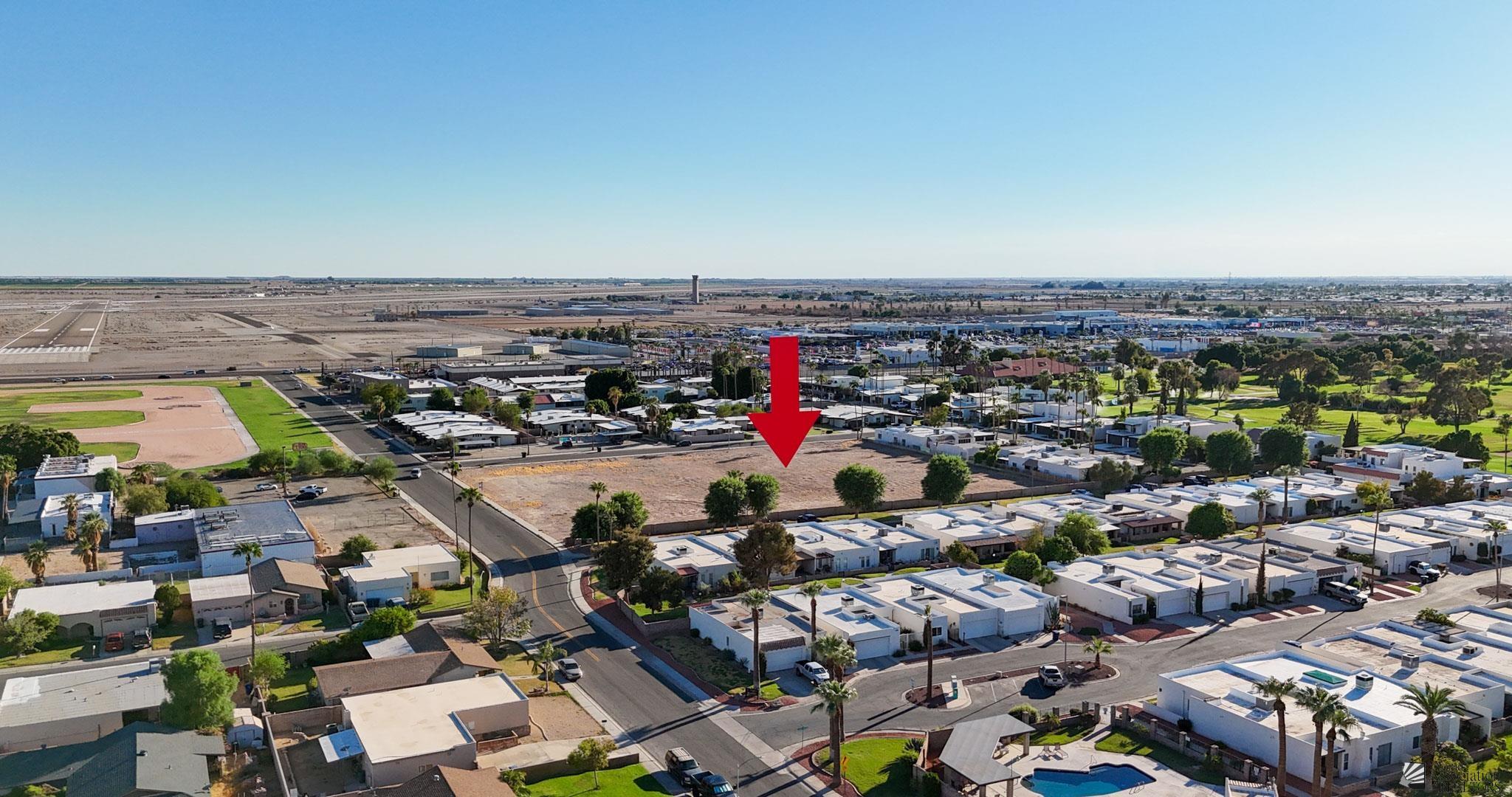 Vacant lot marked by a red arrow amid Yuma homes and streets, with an airport runway in the distance.