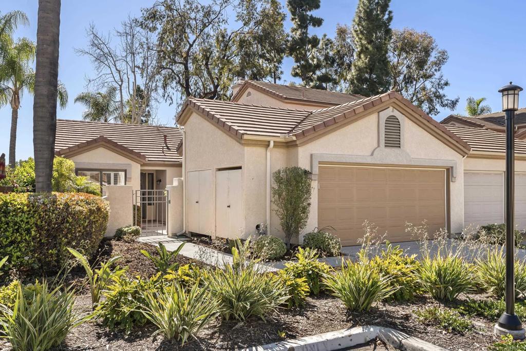 Beige stucco home with a double garage, tile roof, and landscaped front garden.