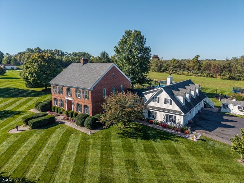 Aerial view of a brick house beside a white house, surrounded by striped lawns and open fields.