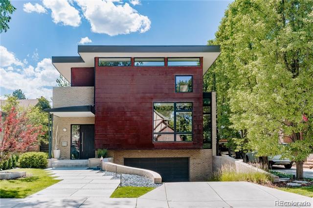 Modern red-clad home with large windows, a garage, and a concrete driveway.