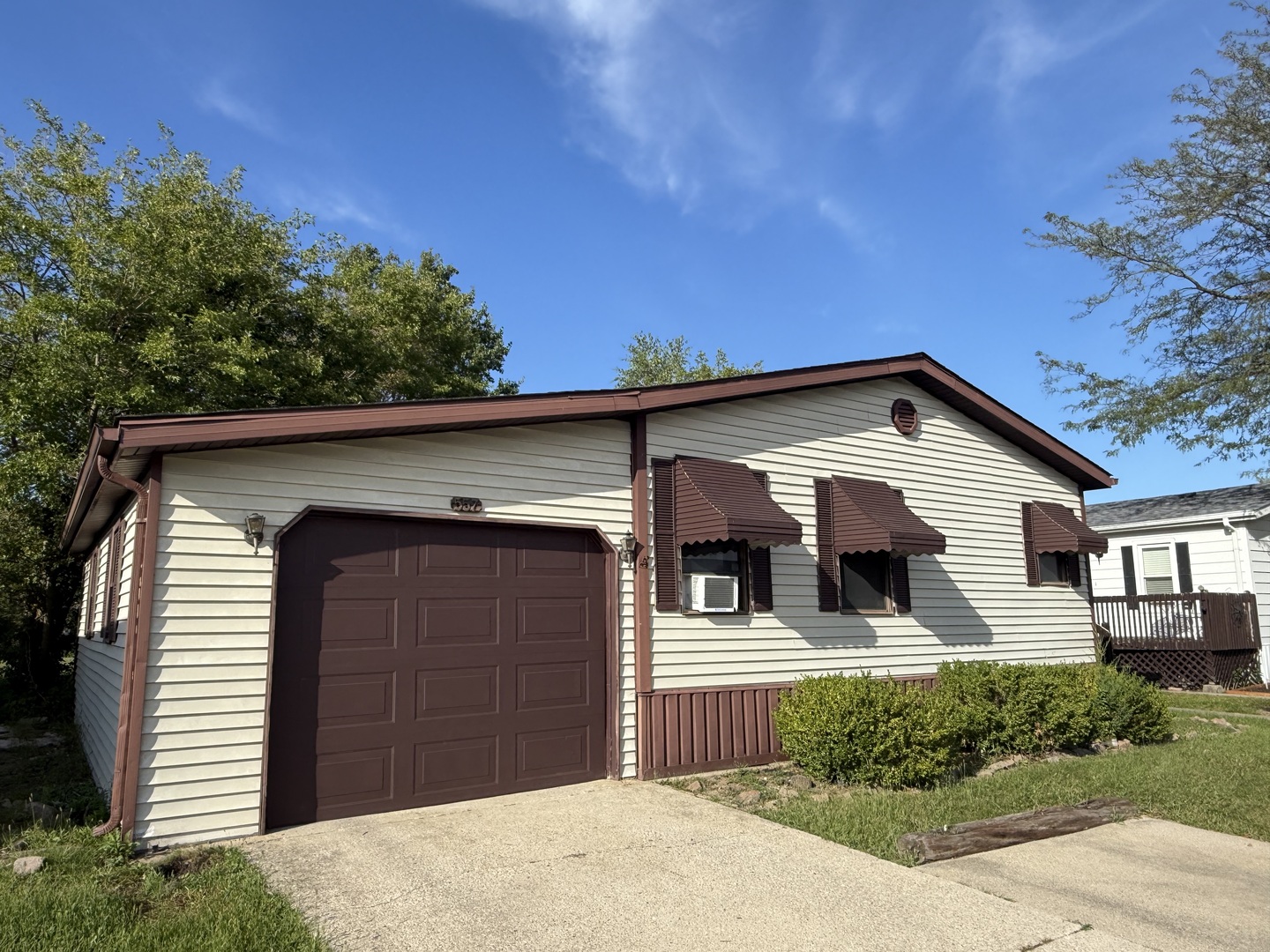 Single-story house with burgundy garage door and awnings beside a concrete driveway.
