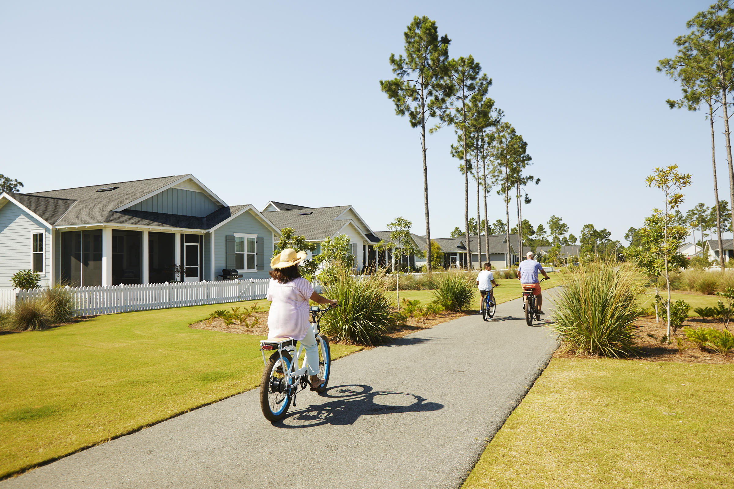 Residential street lined with homes as cyclists ride along a landscaped paved path.