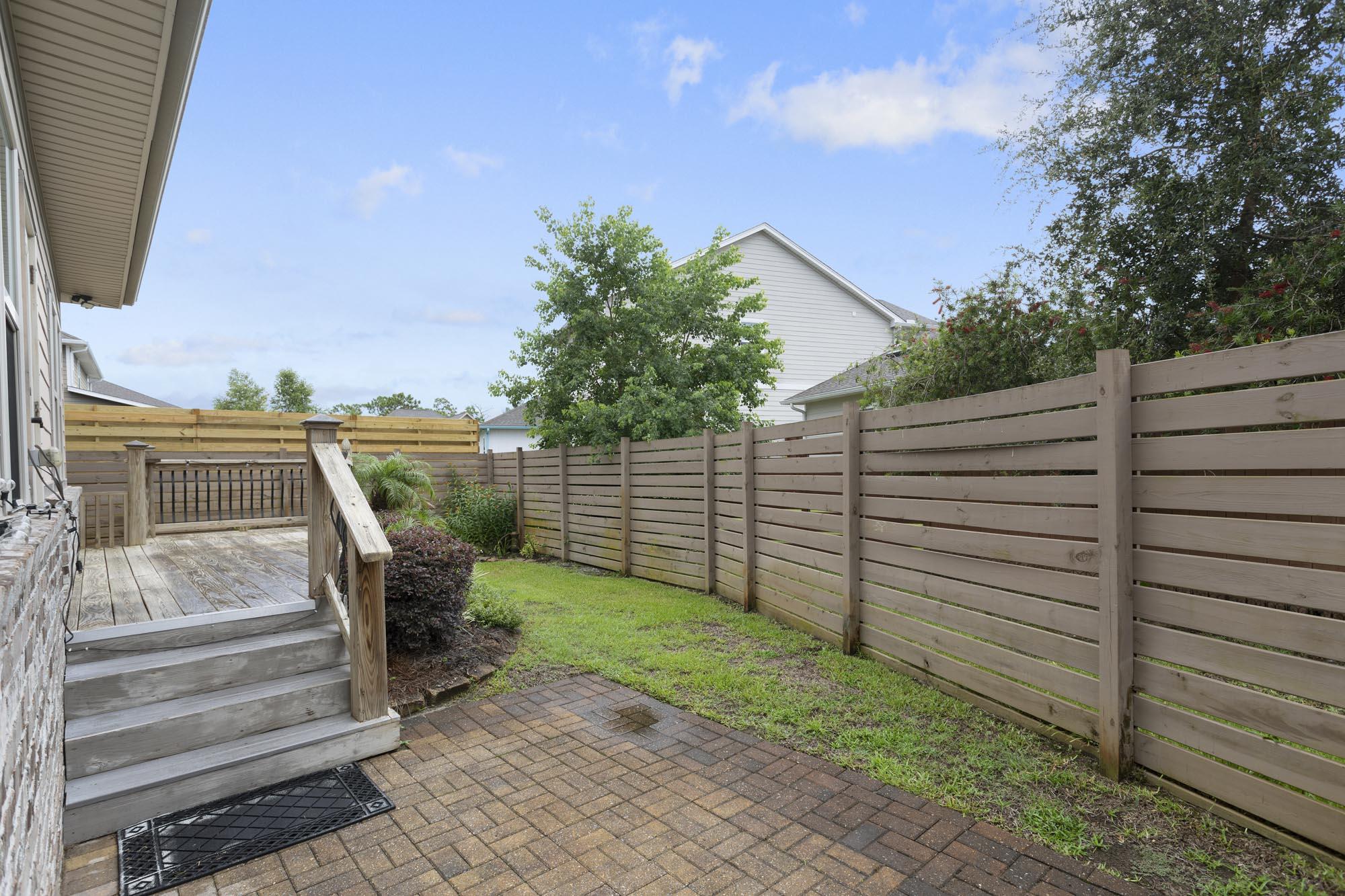 Fenced backyard with a brick patio, wooden deck and steps, and a small lawn.