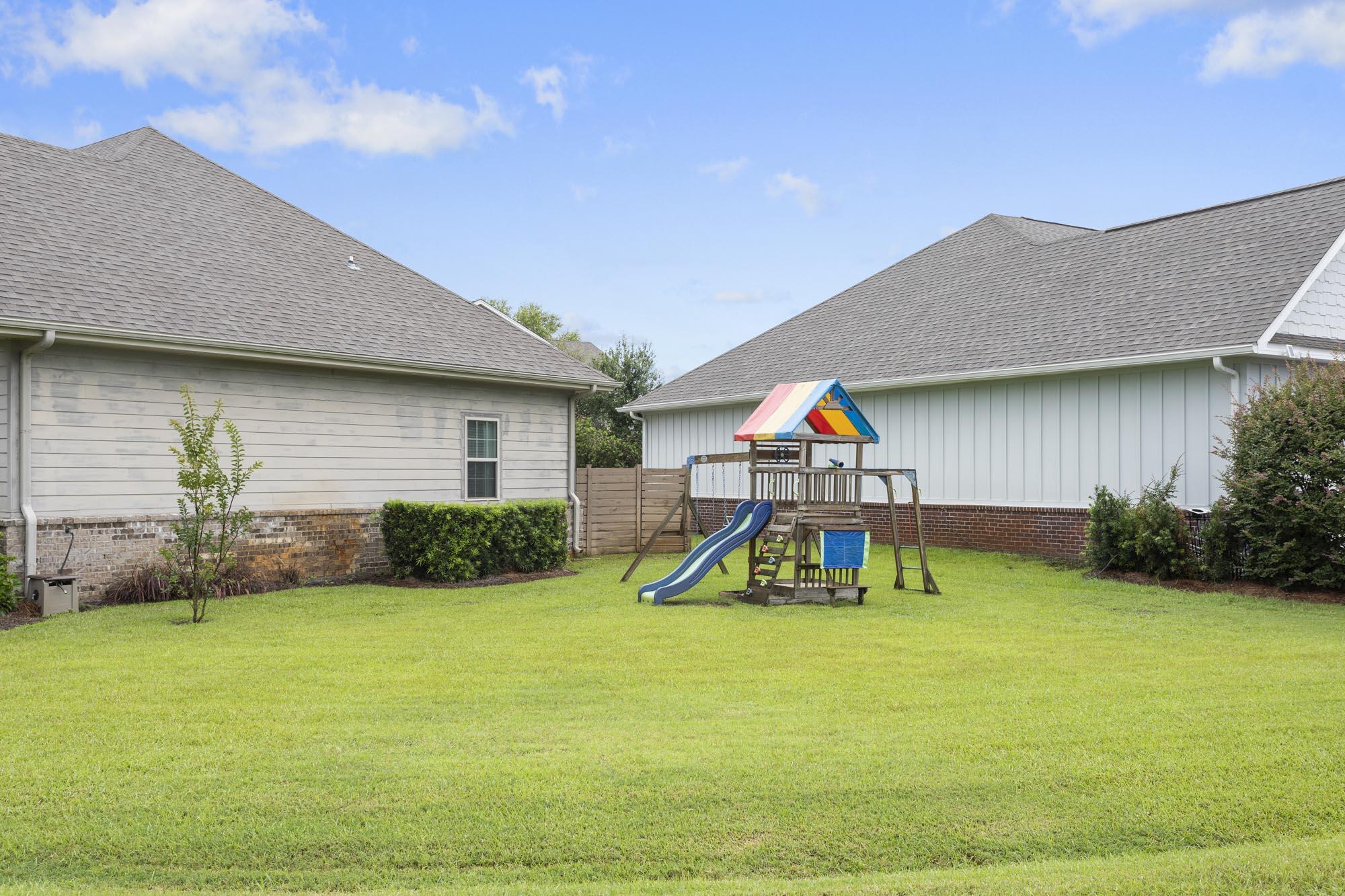 Grassy backyard with a colorful playset and slide between the home's rear wings.
