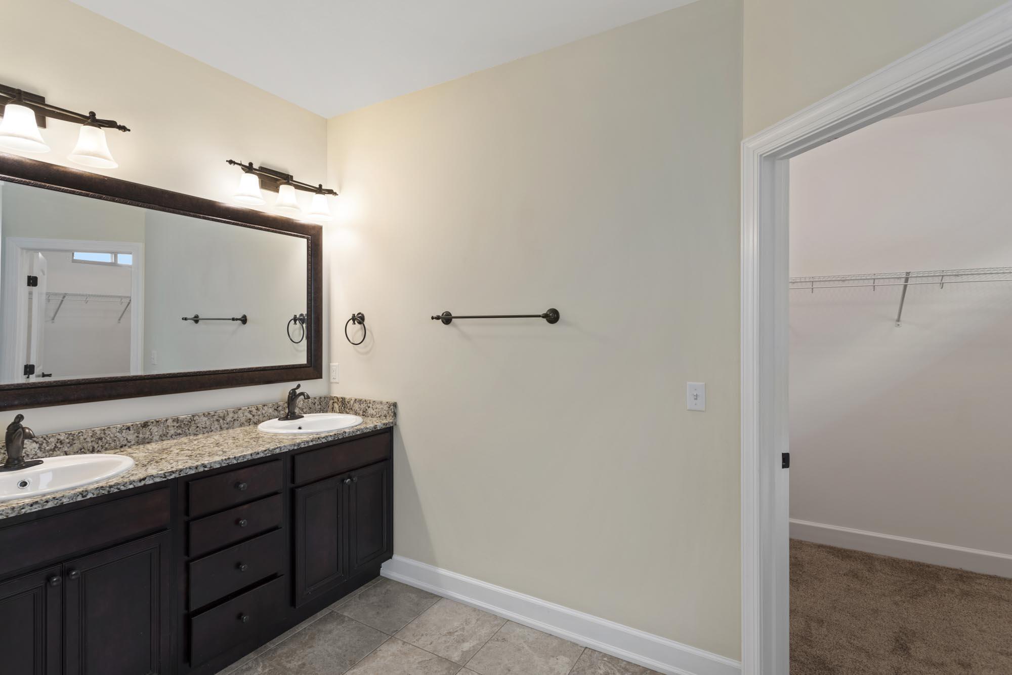 Bathroom with a dark double vanity and stone countertop beside an open walk-in closet.