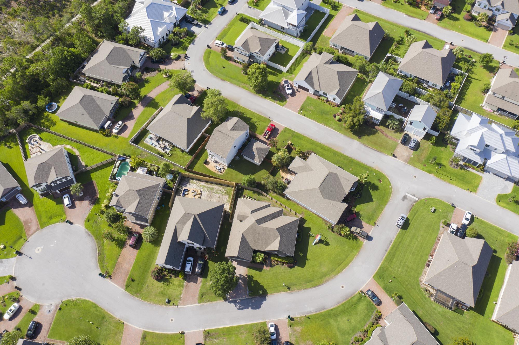Aerial view of homes along a curved residential street, with green lawns and backyard pools.