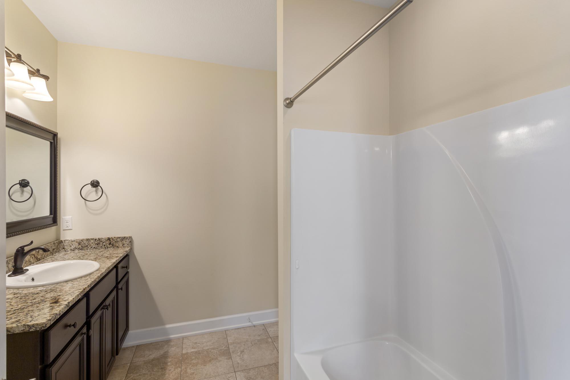 Bathroom with a white tub and shower beside a dark wood vanity with granite countertop.