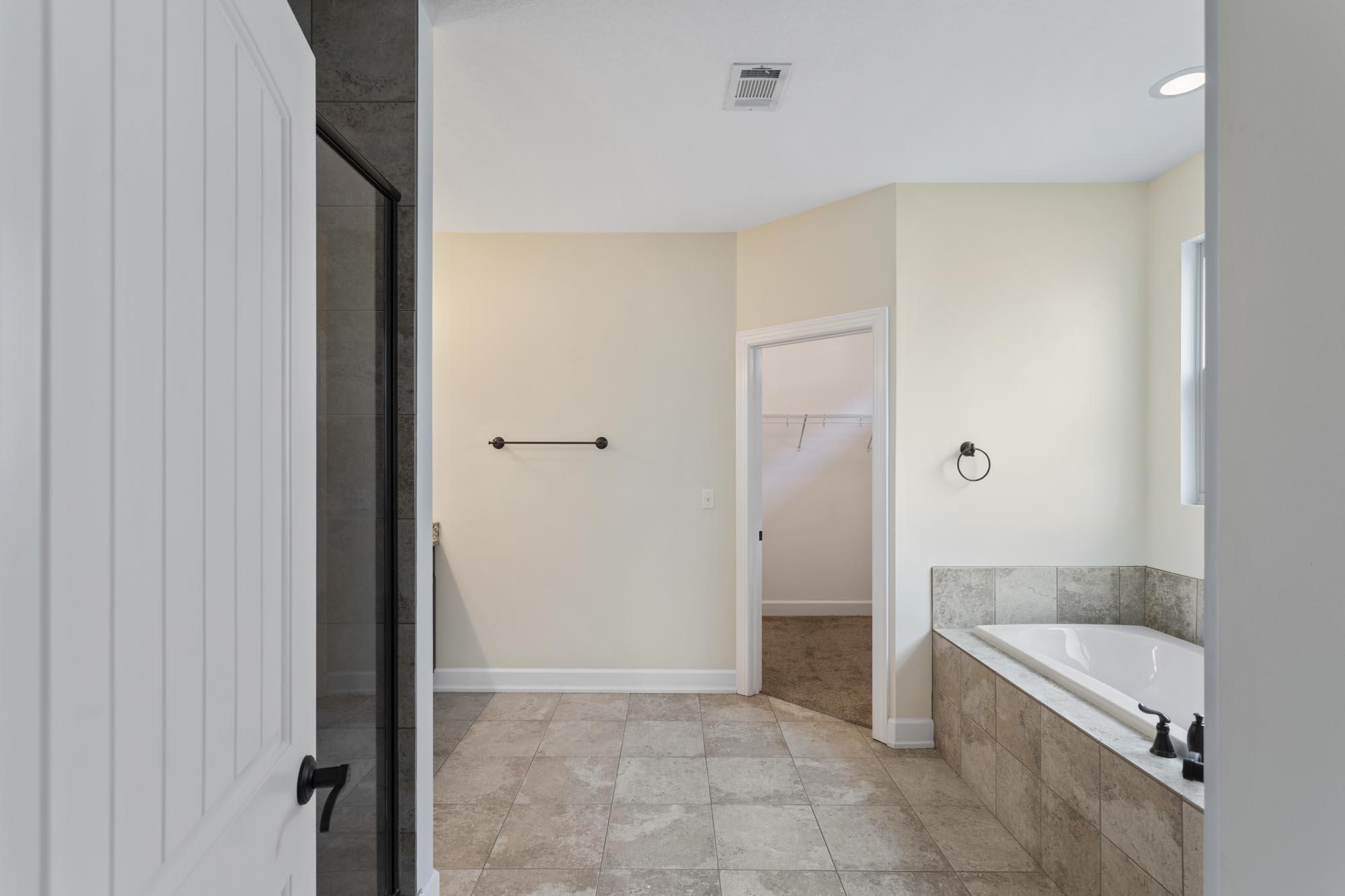Bathroom with a tiled soaking tub, glass shower, and doorway to a walk-in closet.