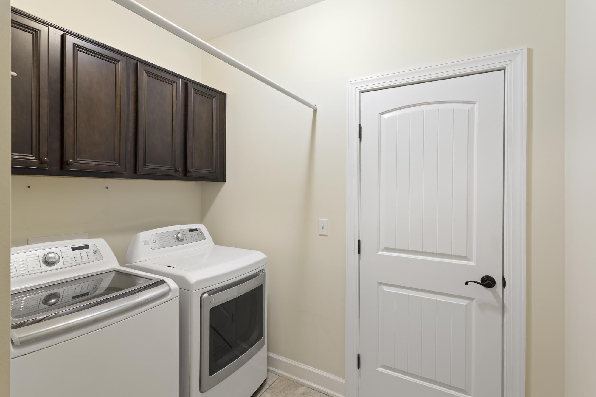 Laundry room with washer and dryer beneath dark wood cabinets, beside a white paneled door.