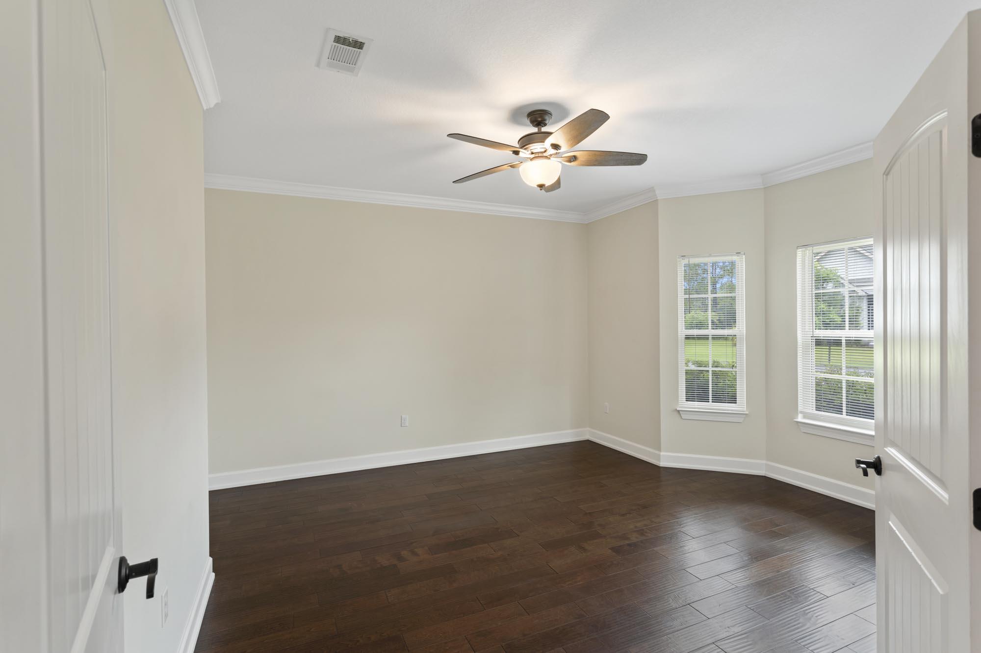 Empty room with dark hardwood floors, two windows, and a ceiling fan with a light.