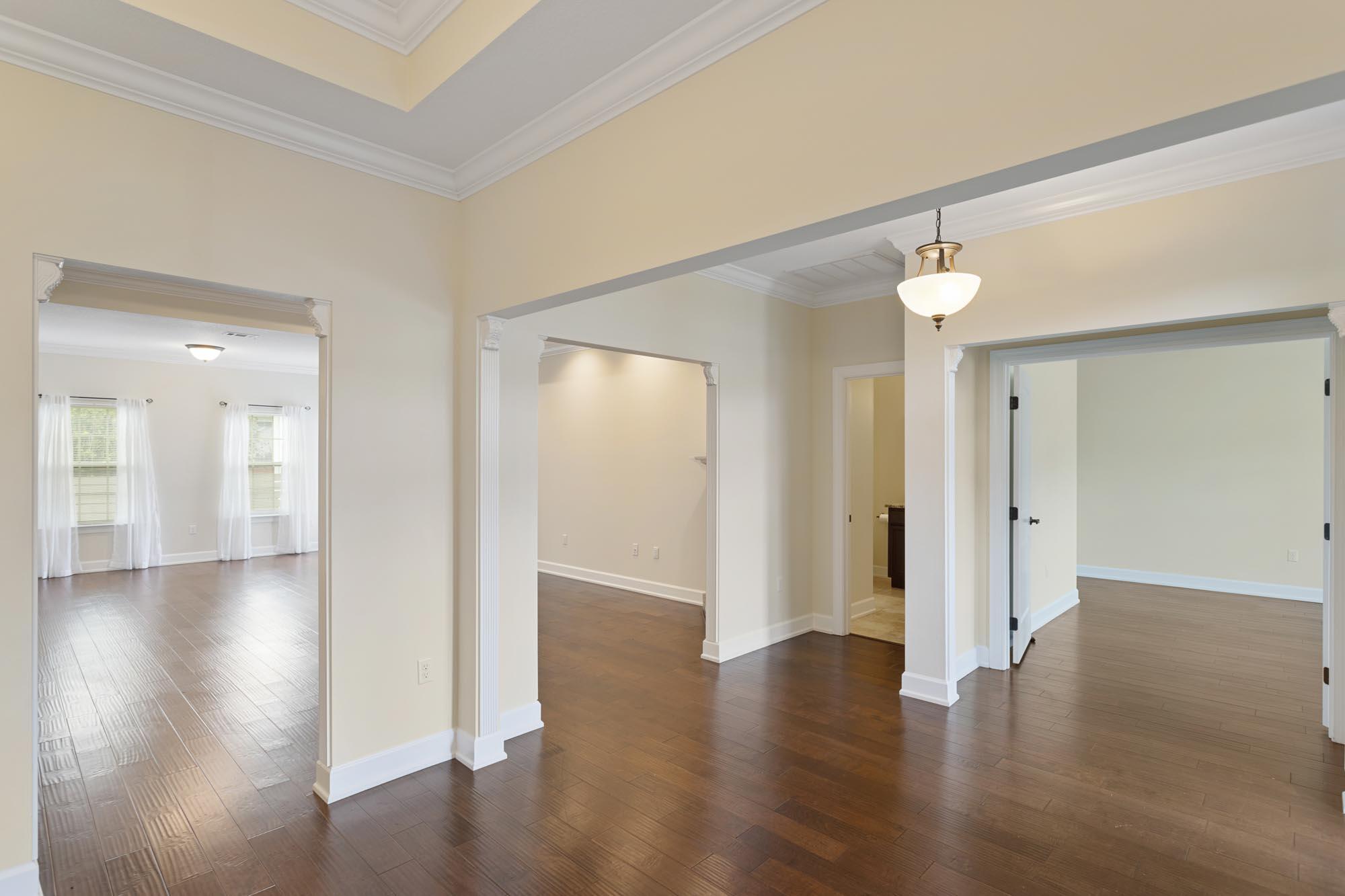Vacant interior with hardwood floors, a tray ceiling, and wide openings between rooms.
