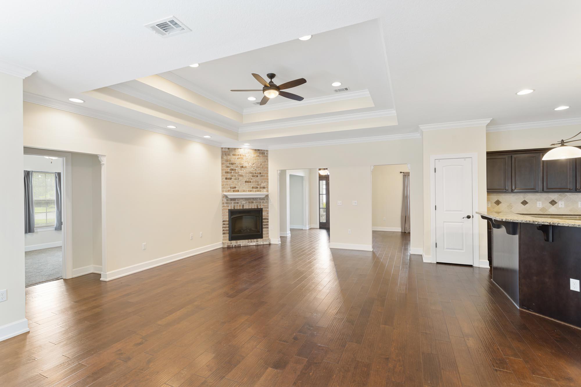 Open living area with wood floors, brick fireplace, tray ceiling, and adjoining kitchen island.