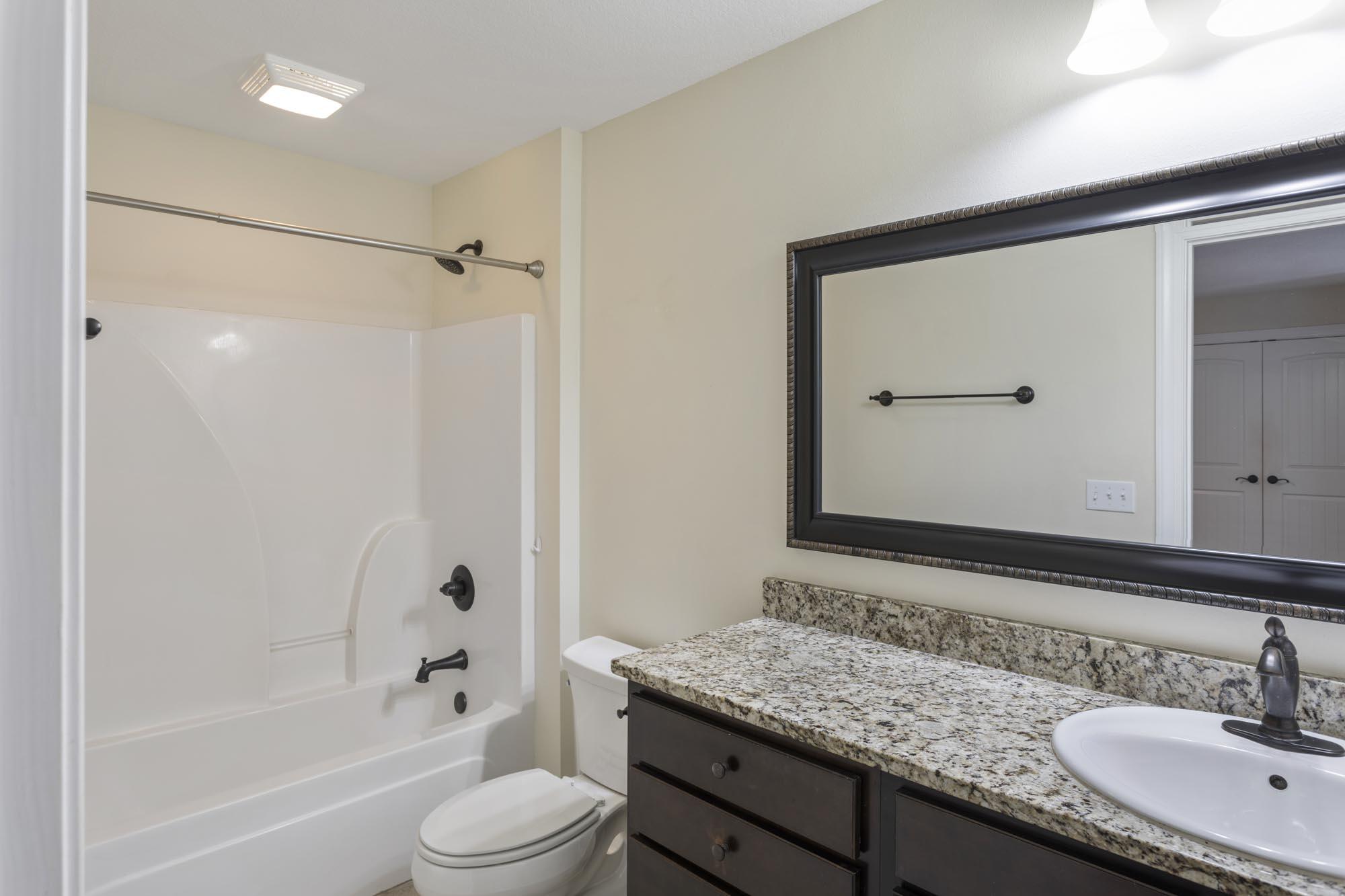 Bathroom with a white tub-shower and toilet beside a dark vanity with a granite countertop.