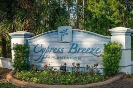 Cypress Breeze at Plantation entrance sign framed by white pillars and tropical landscaping.