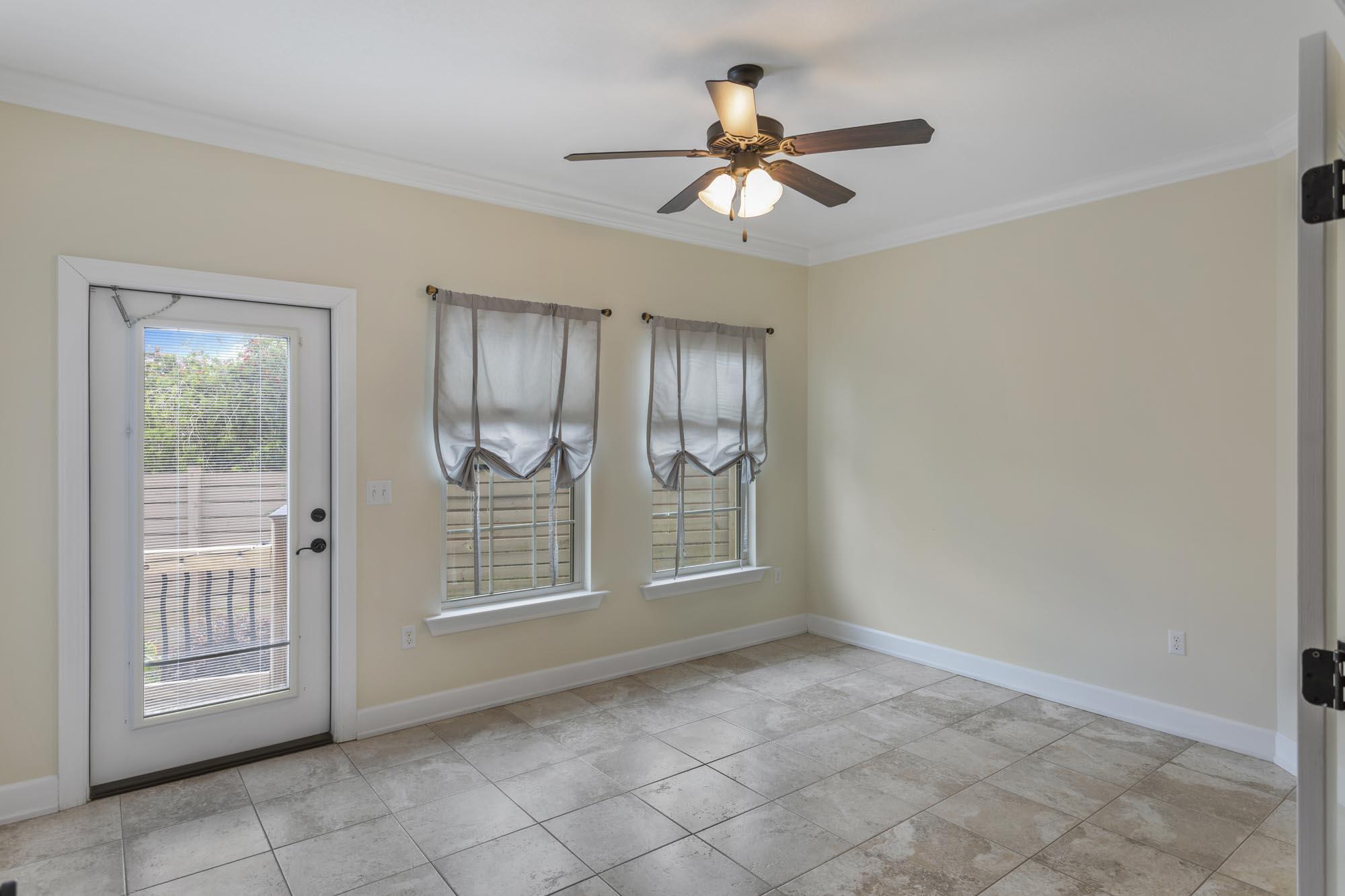 Empty tiled room with two curtained windows, a glass-paneled door, and a ceiling fan.