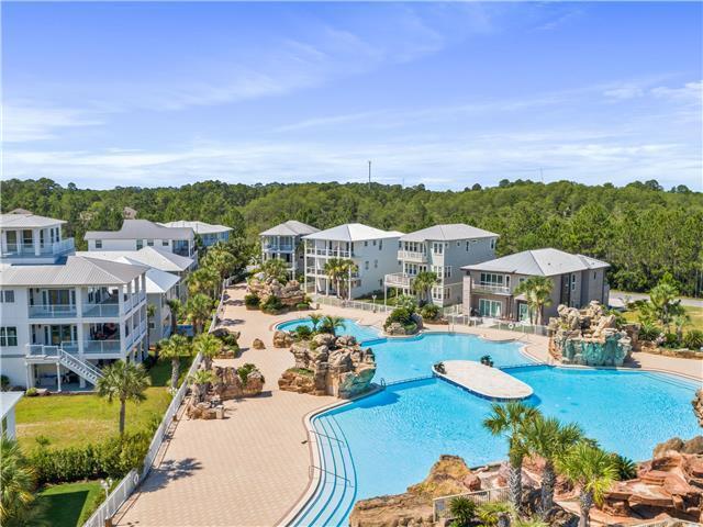 Aerial view of a community pool with rock landscaping and multi-story homes nearby.