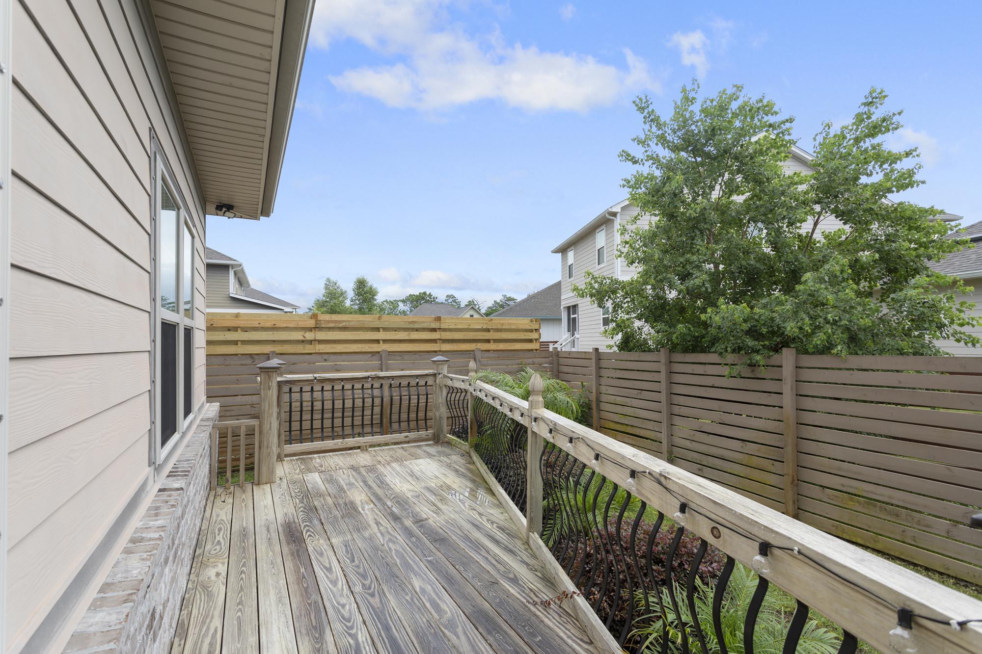 Raised wooden deck with black metal railings and privacy fencing beside a light-sided home.