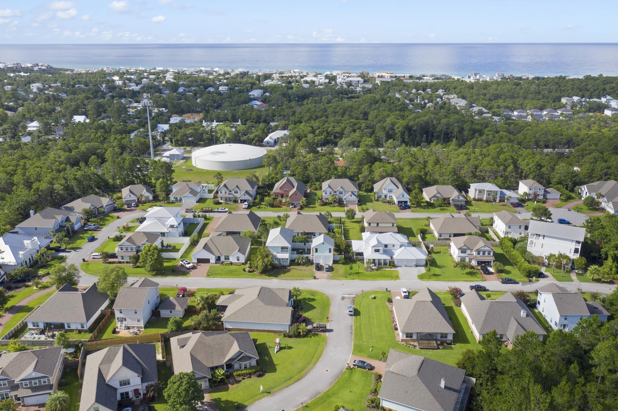 Aerial view of homes along a curving street, with wooded areas and the Gulf beyond.