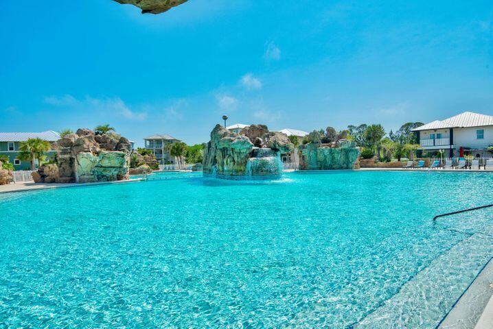 Outdoor pool with turquoise water and rock waterfalls, surrounded by houses.