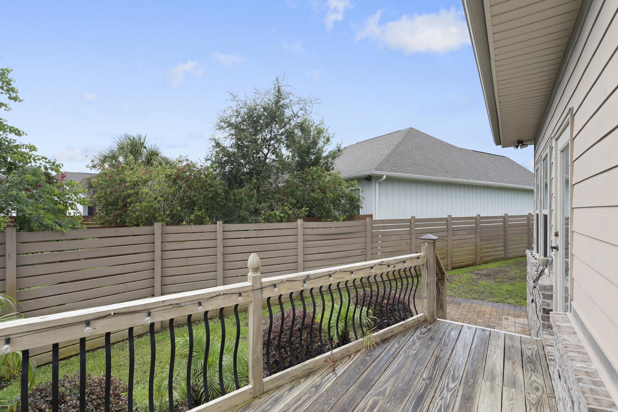 Wood deck with railing and string lights overlooking a fenced, landscaped yard.