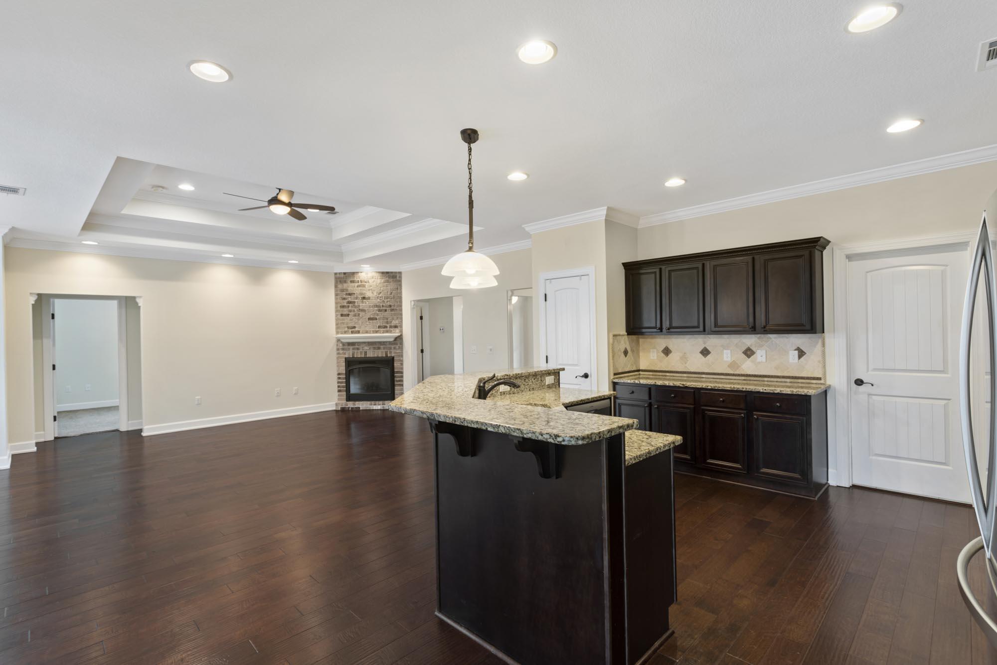 Unfurnished kitchen with dark cabinets, granite counters, and a peninsula opening to a living area with a brick fireplace.