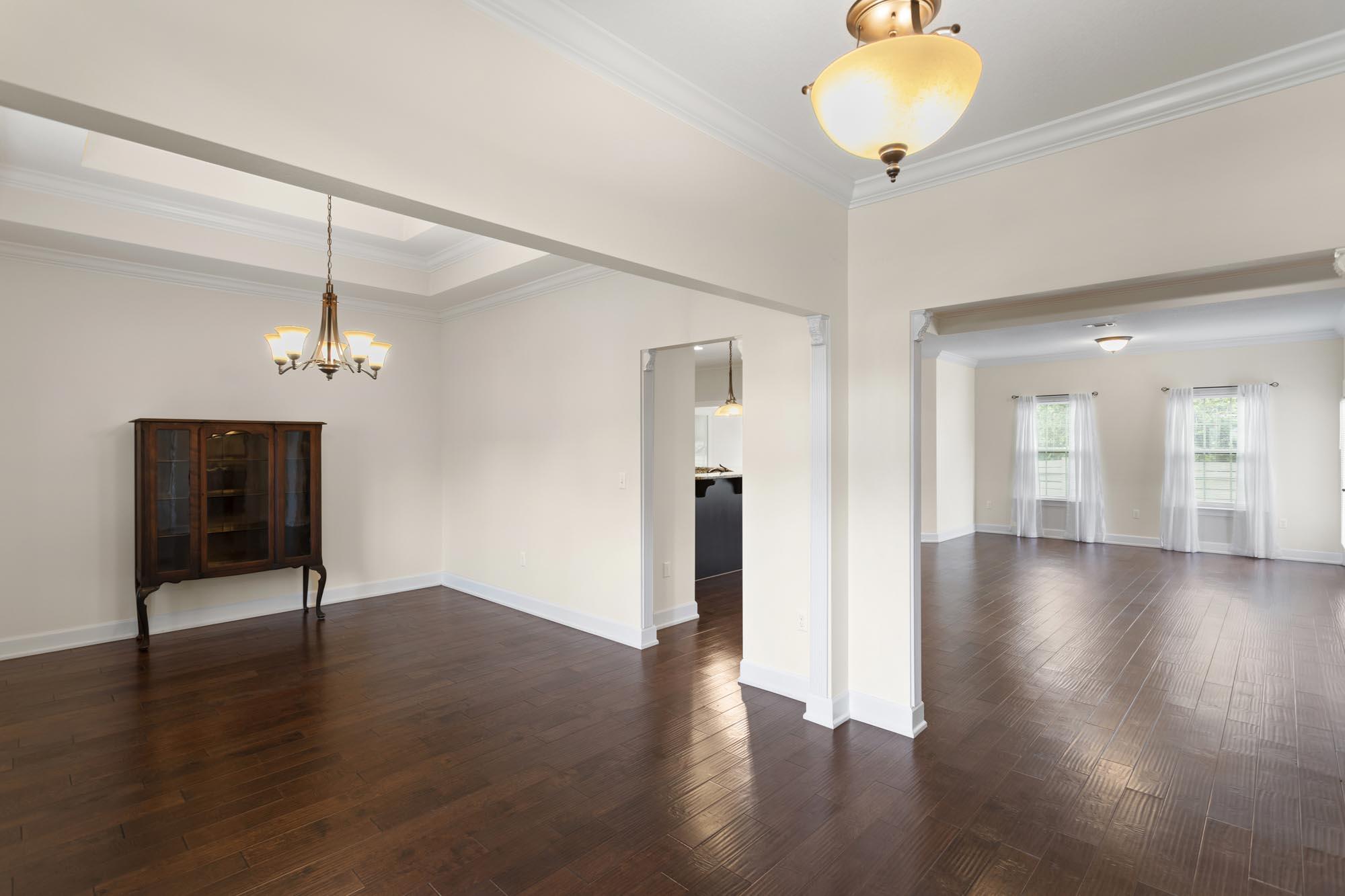 Dining room with dark wood floors, a tray ceiling, chandelier, and adjoining sunlit room.