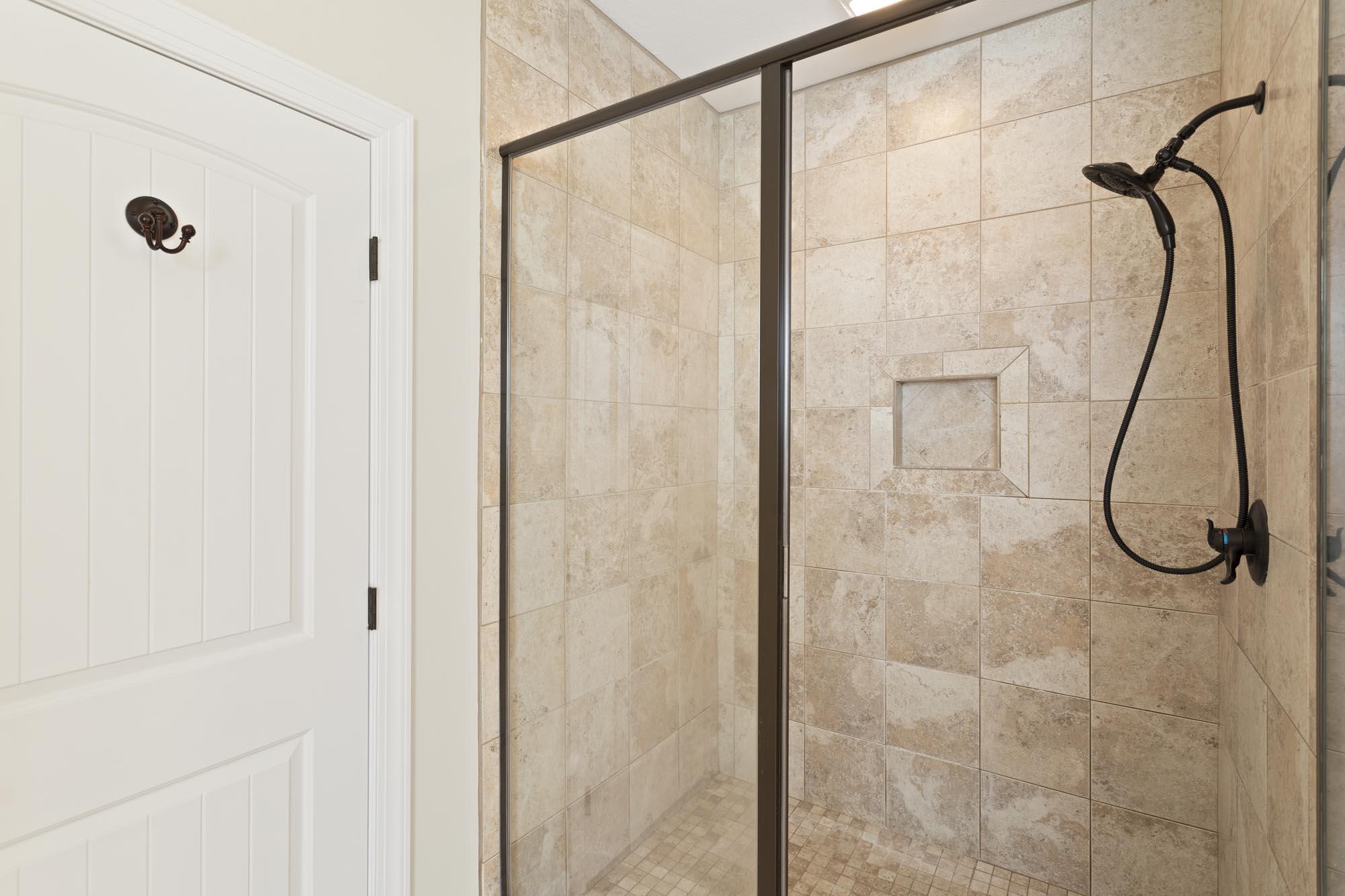 Tiled walk-in shower with dark metal framing, handheld showerhead, and recessed wall niche.