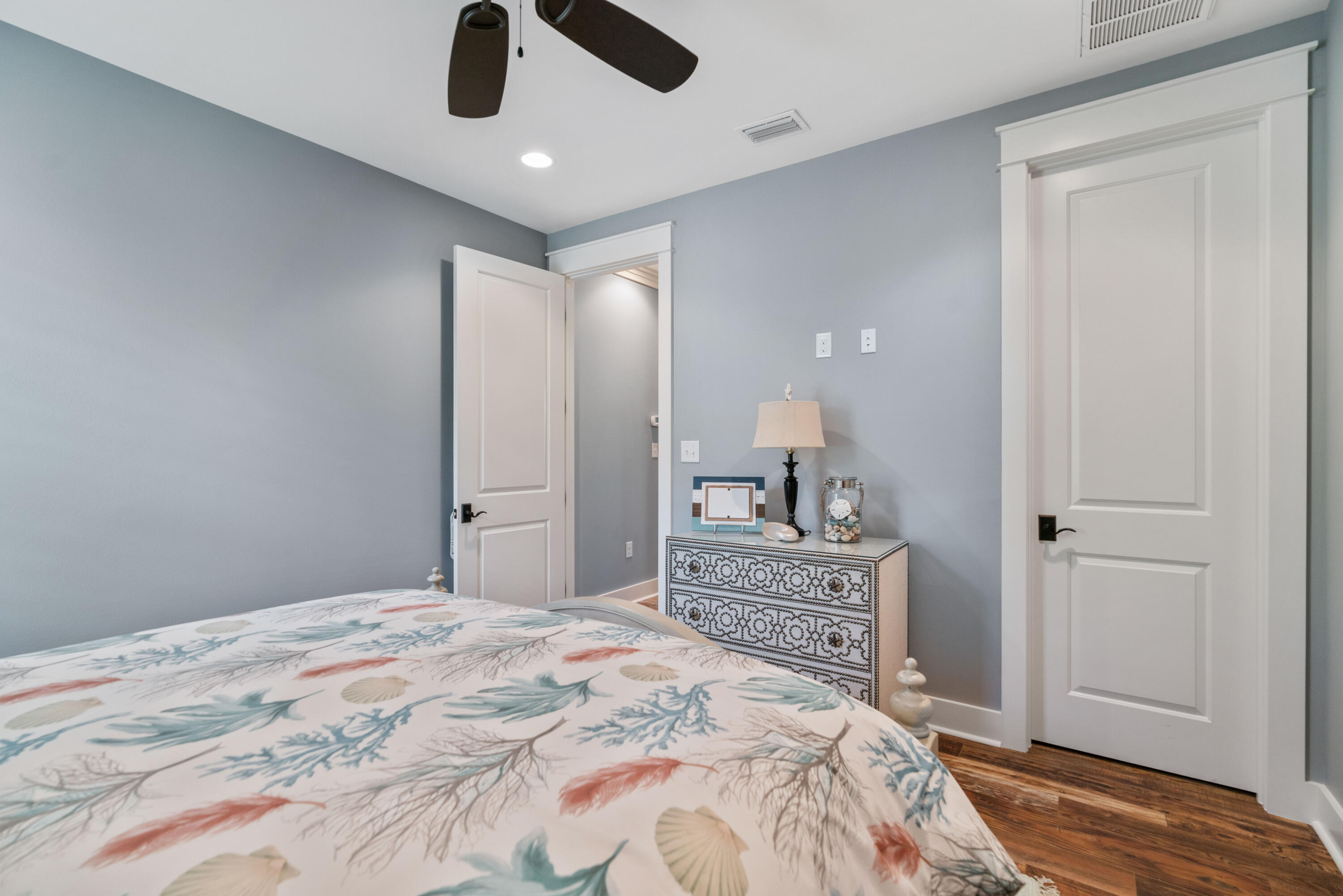 Bedroom with a botanical-print bedspread and ornate dresser against pale blue-gray walls.