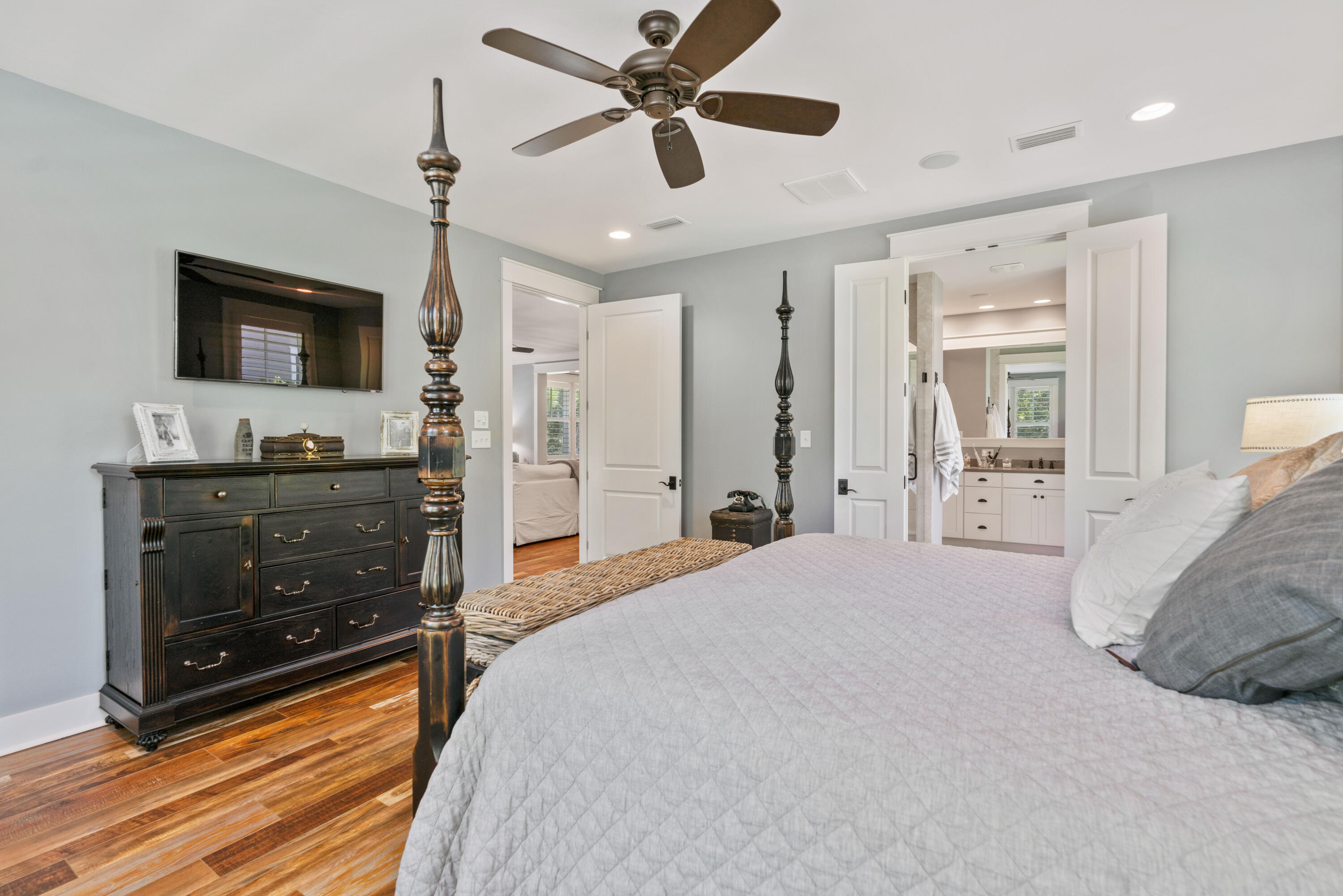 Bedroom with a four-poster bed, dark wood dresser, and open doorway to an en suite bathroom.