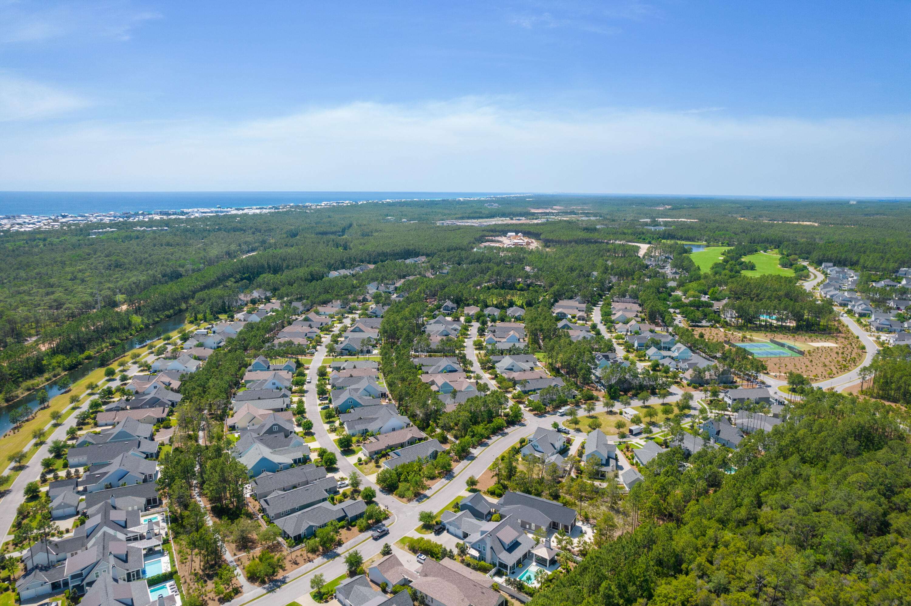Aerial view of a wooded coastal neighborhood, with the ocean on the horizon and a golf course nearby.