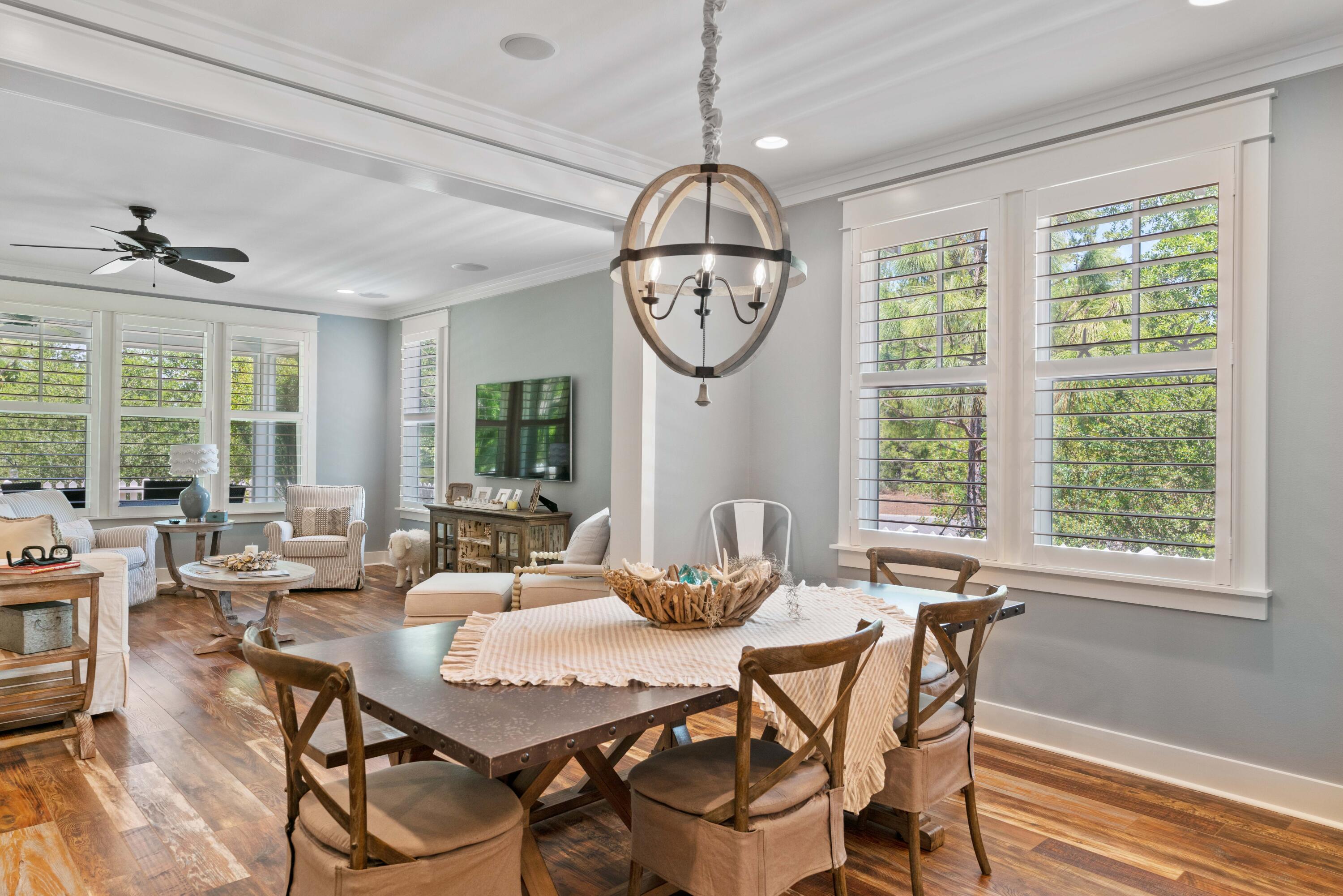 Dining and living room with a rustic wood table, plantation-shuttered windows, and hardwood floors.