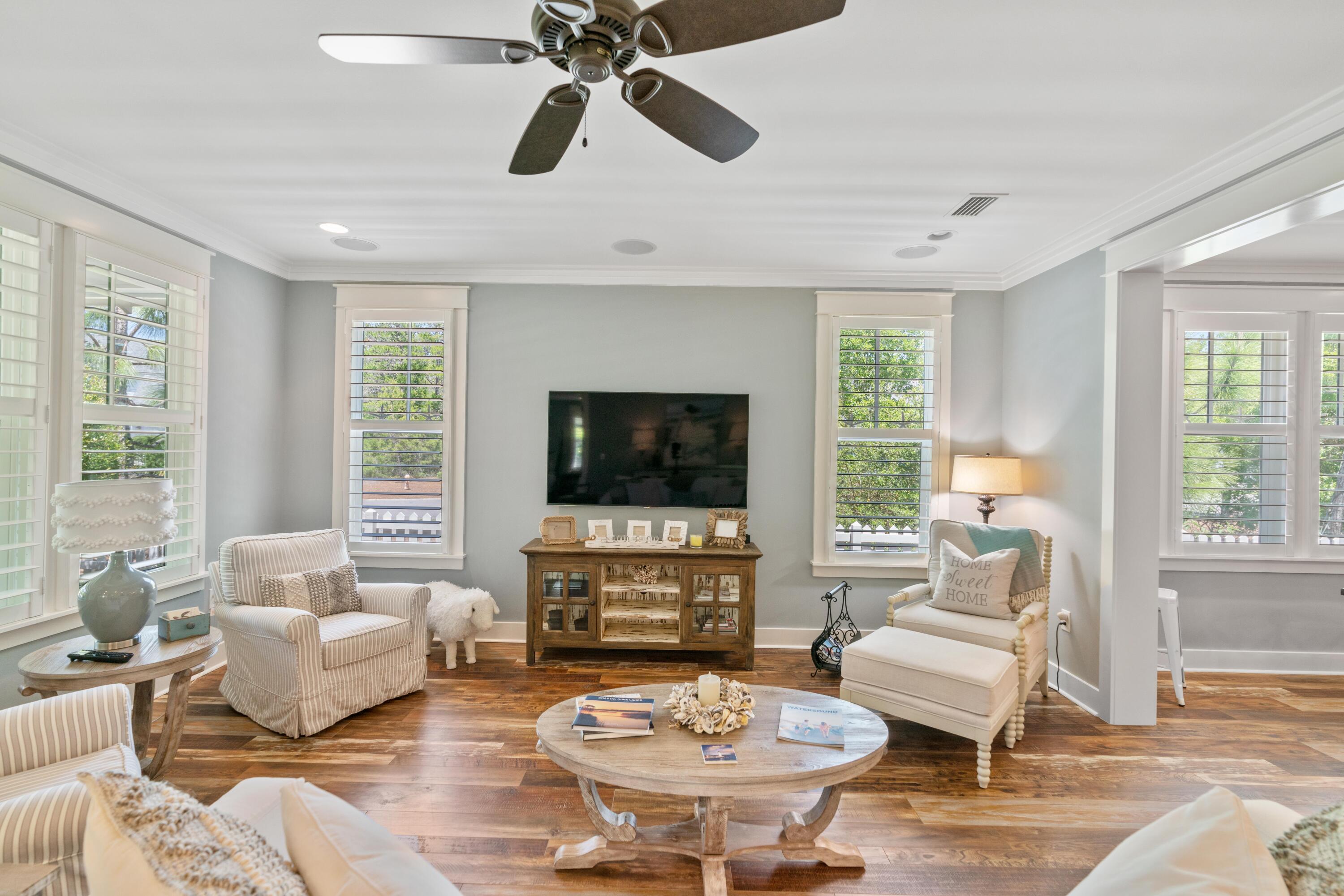 Staged living room with a wall-mounted TV, rustic console, plantation shutters, and warm wood flooring.