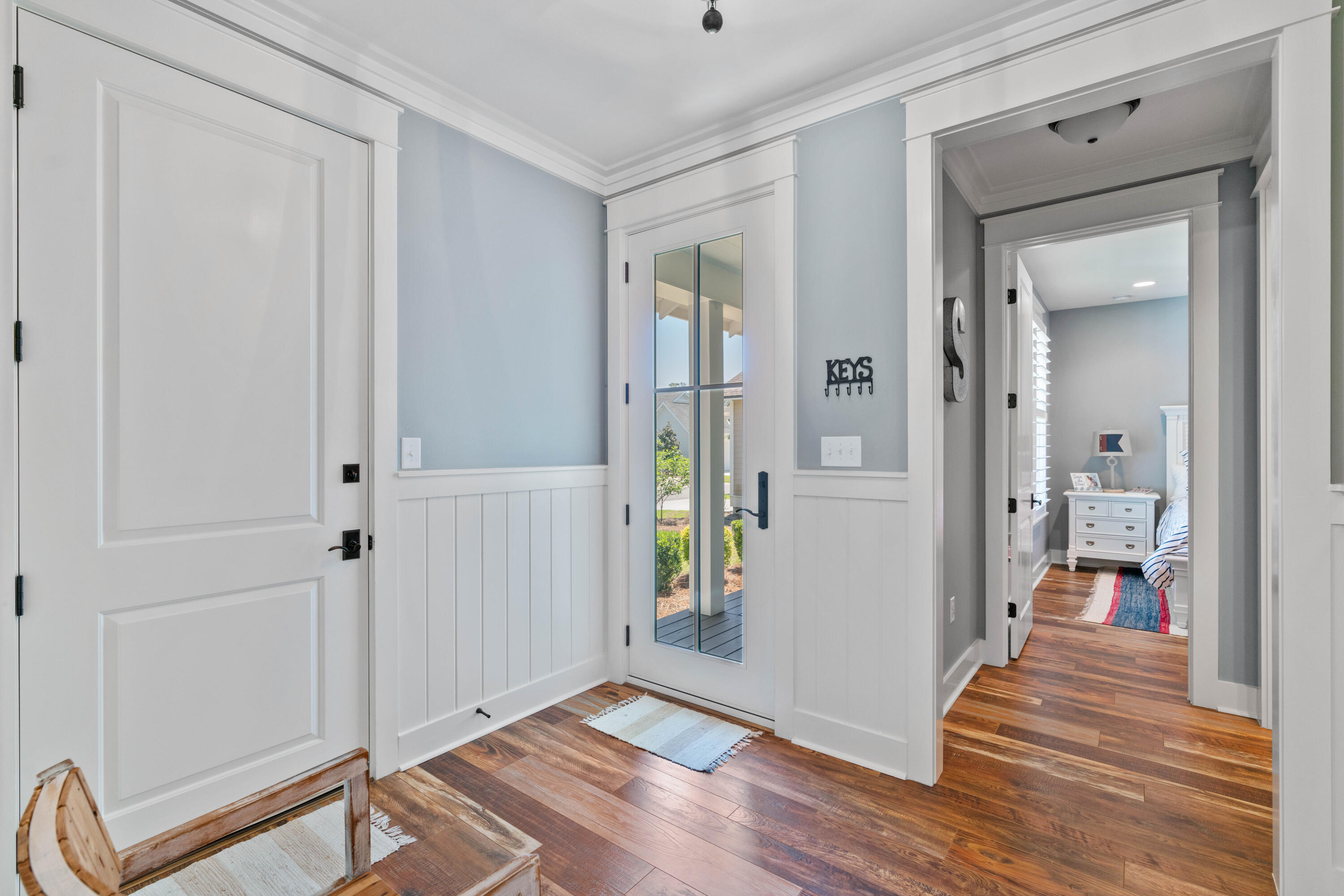 Entry foyer with a glass-paneled door, white wainscoting, and a view into a bedroom.