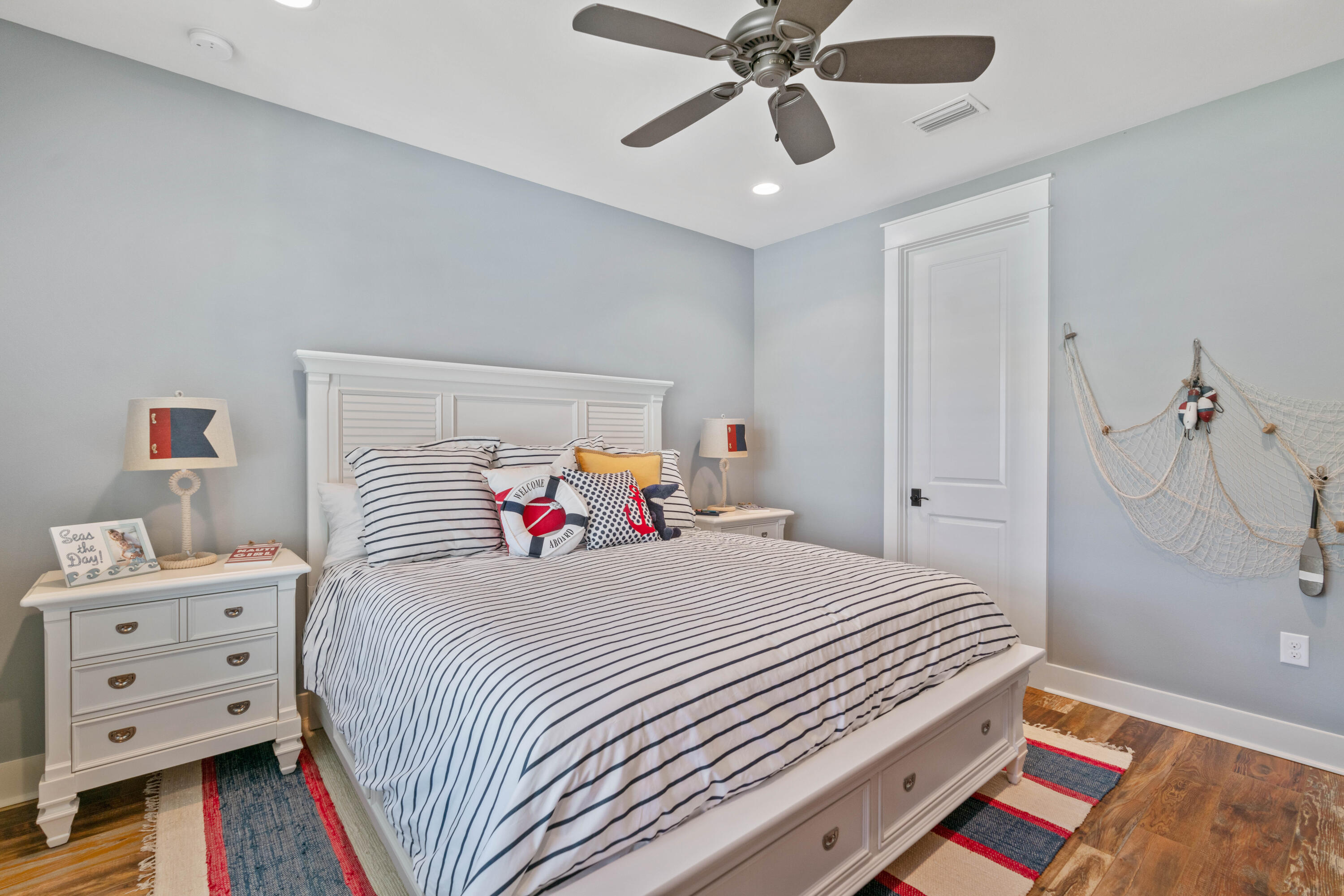 Coastal-themed bedroom with navy-striped bedding, nautical pillows, and fishing-net wall decor.