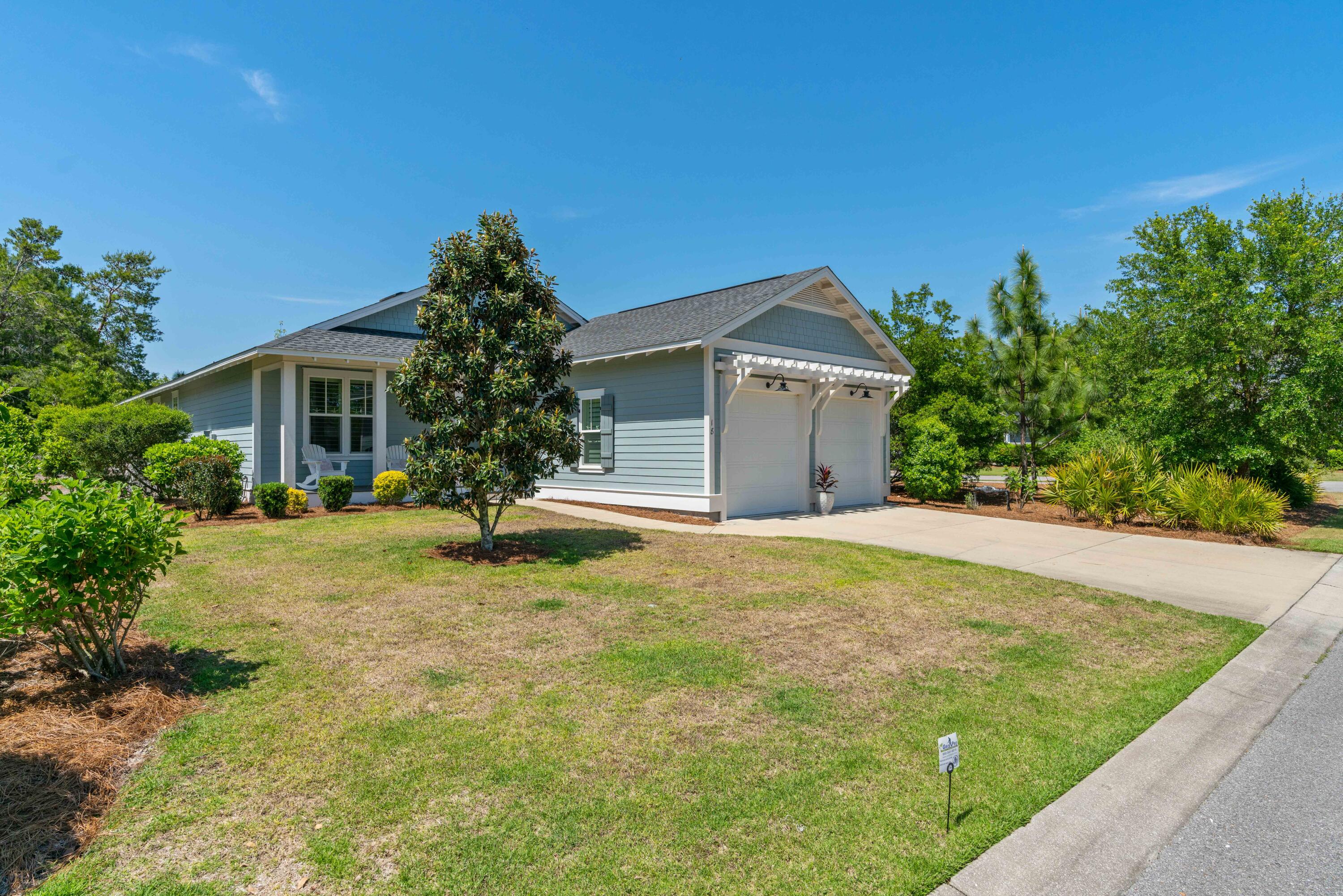 Light blue home with white trim and a two-car garage, framed by a landscaped lawn and mature trees.