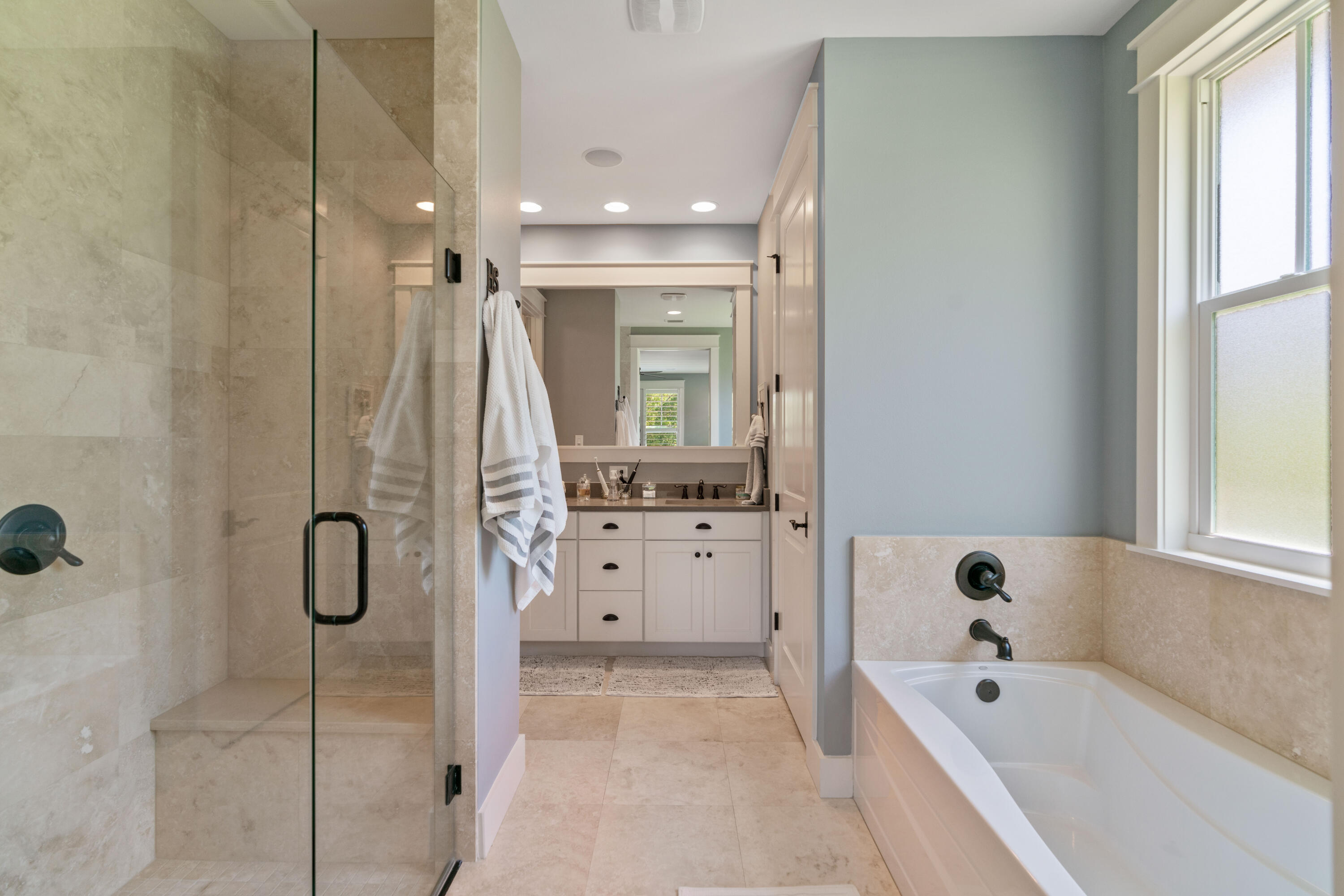 Bathroom with a glass shower, white soaking tub, and pale stone tile.
