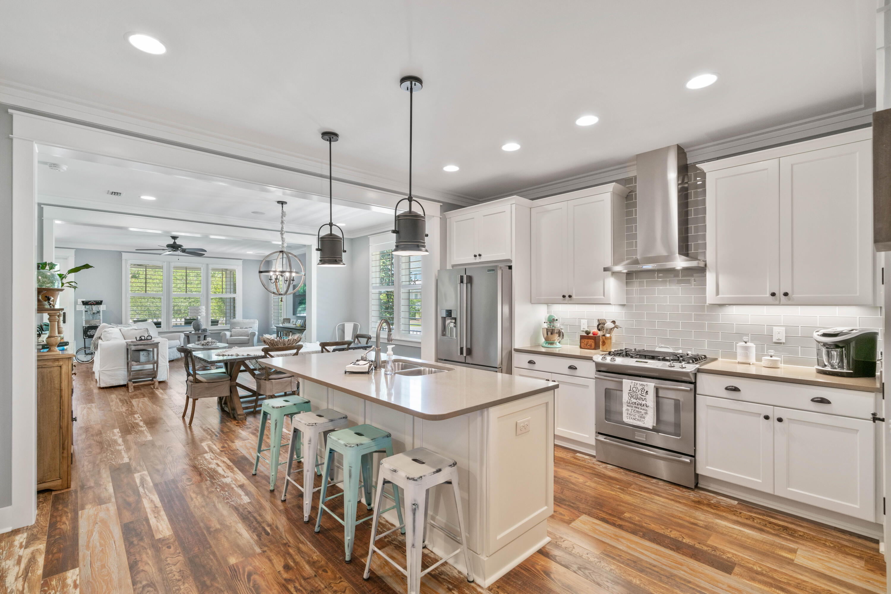 Open-plan kitchen with white cabinets, stainless steel appliances, and a large island opening to a furnished living room.